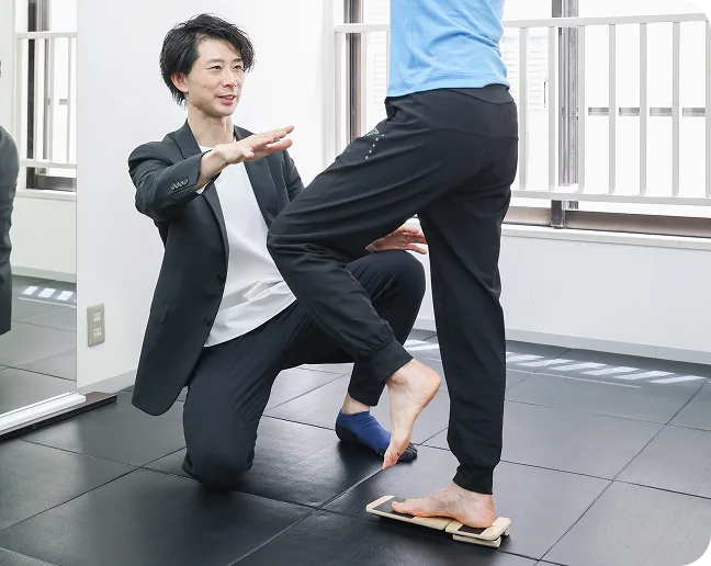 トレーナーが、バランスボードに乗ったお客様の足元を指導している様子